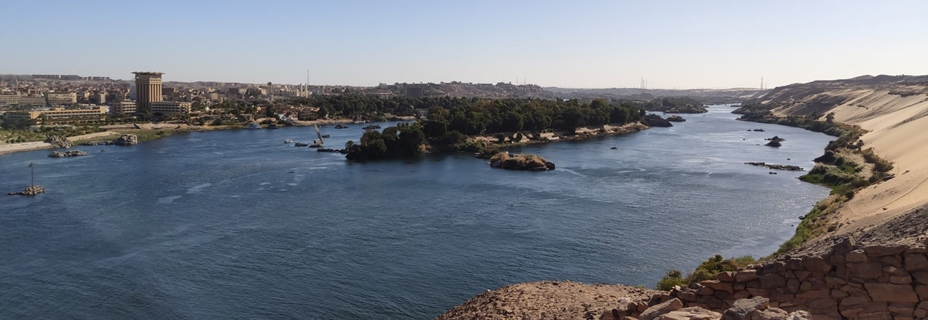 Scenic view of the Nile River in Aswan with traditional Feluccas and desert dunes.