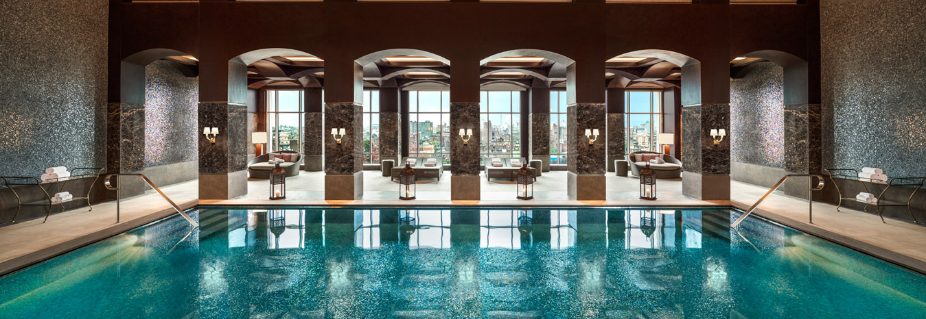 Outdoor luxury swimming pool at the St. Regis Cairo Hotel with comfortable lounge chairs and a view of the city skyline.