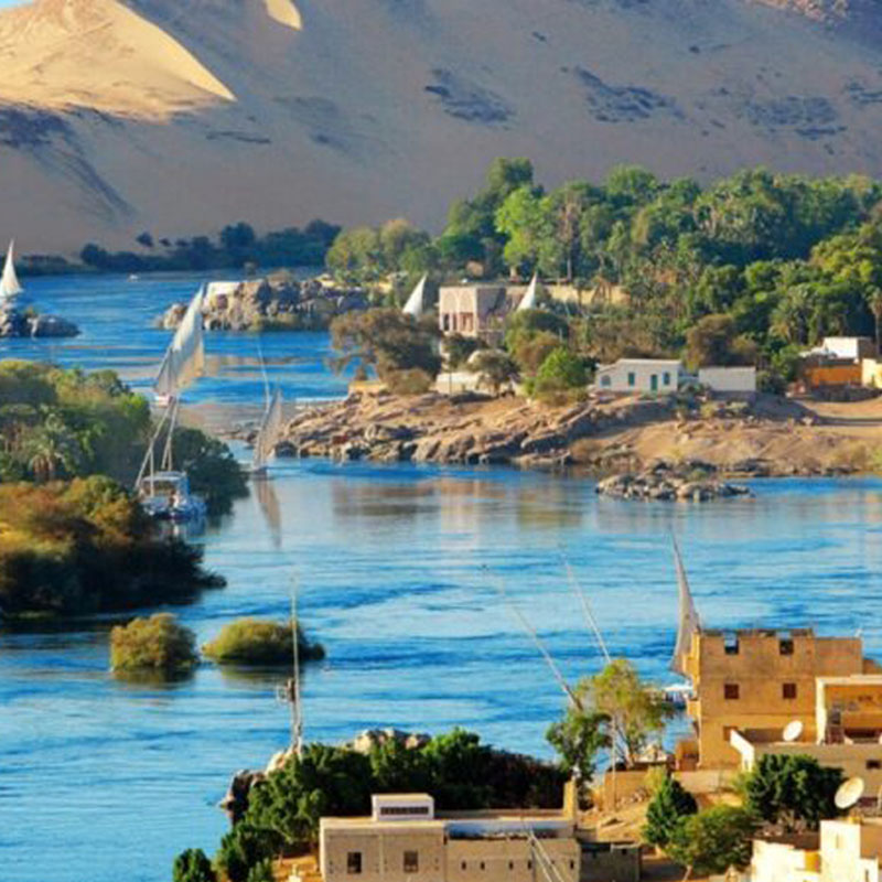 Scenic view of the Nile River in Aswan with traditional sailing boats and desert hills, featured in the 13 Days Wonder of Egypt Tour by Avatar Travel.
