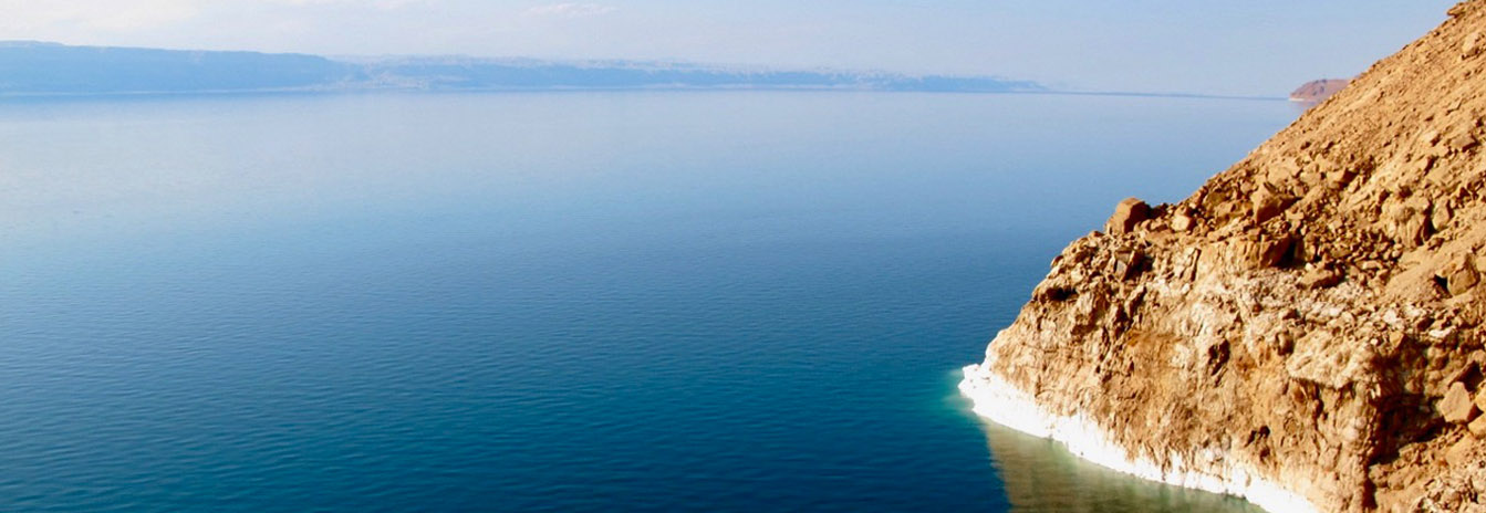 Tourists floating in the turquoise, salt-rich waters of the Dead Sea with desert mountains in the background.
