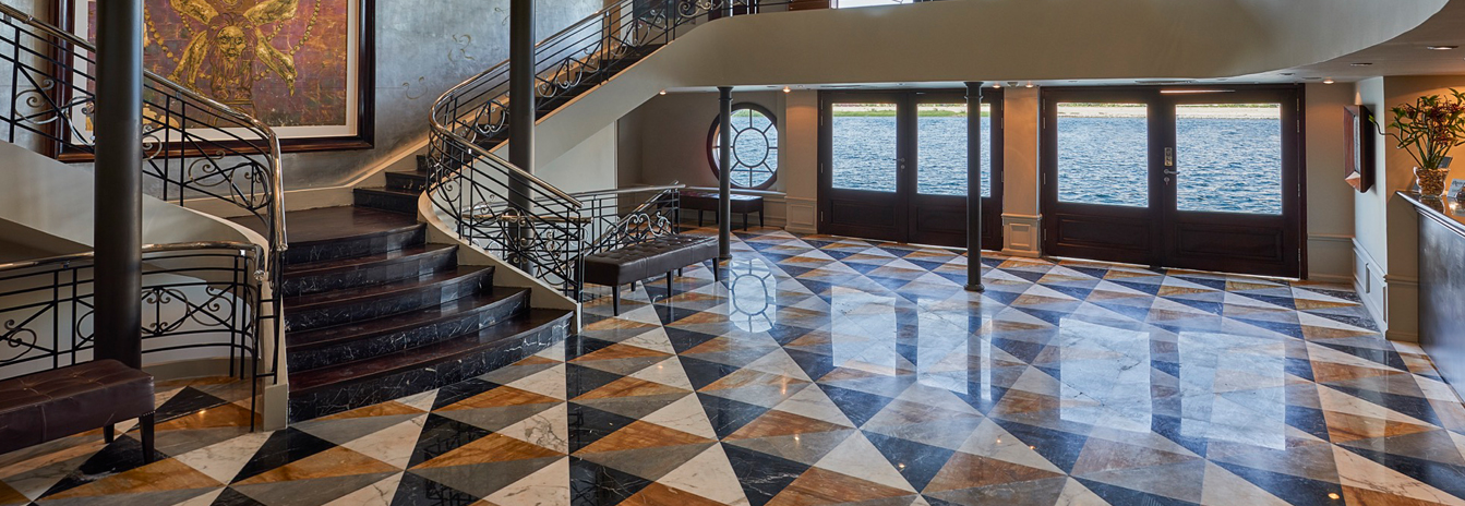 The grand lobby of the Movenpick MS Sunray Nile Cruise featuring a winding staircase, patterned marble floors, and large river-view windows.