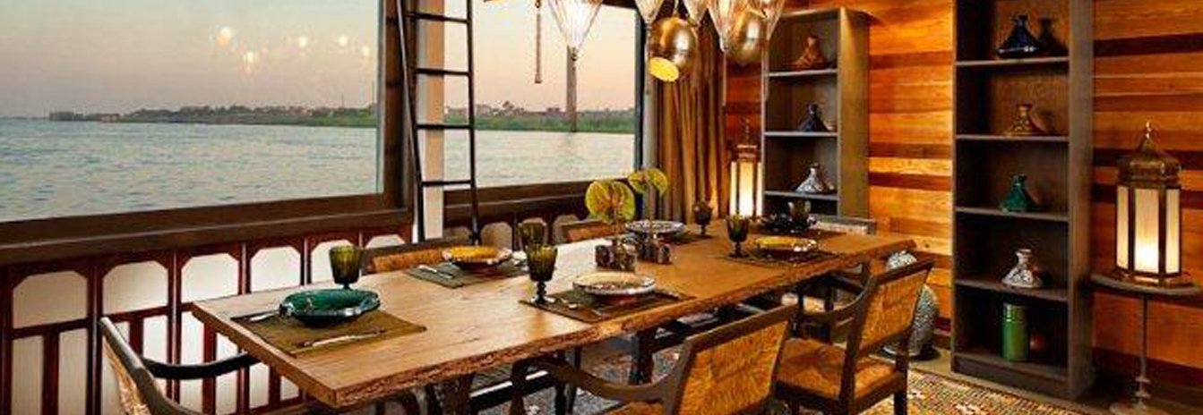 The sophisticated indoor dining room of the Mövenpick SB Feddya boutique vessel with large windows overlooking the Nile.