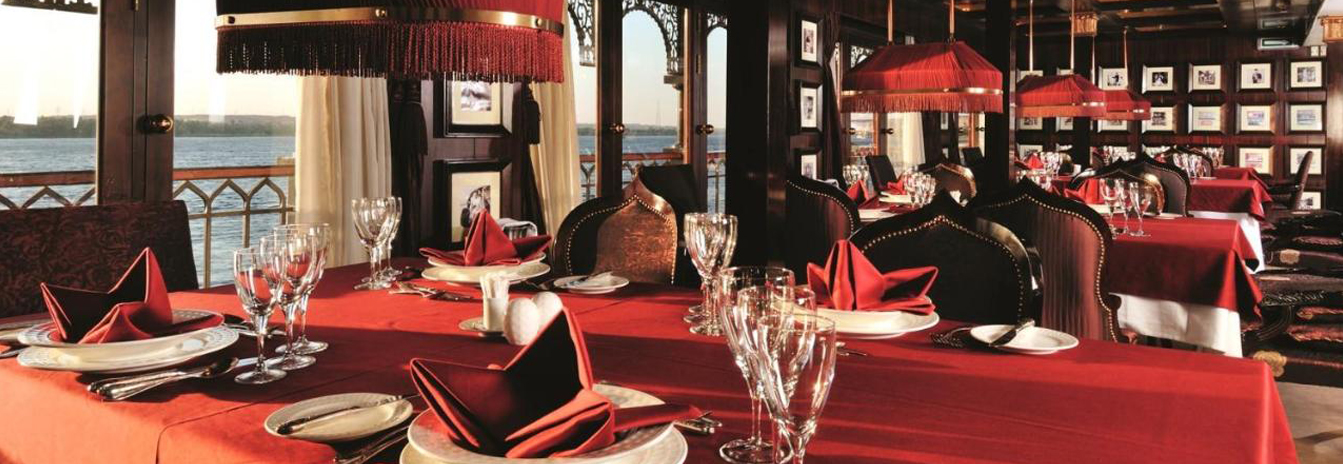 The Marasem Restaurant on the Mövenpick SS Misr featuring red tablecloths, royal portraits, and panoramic Nile views.