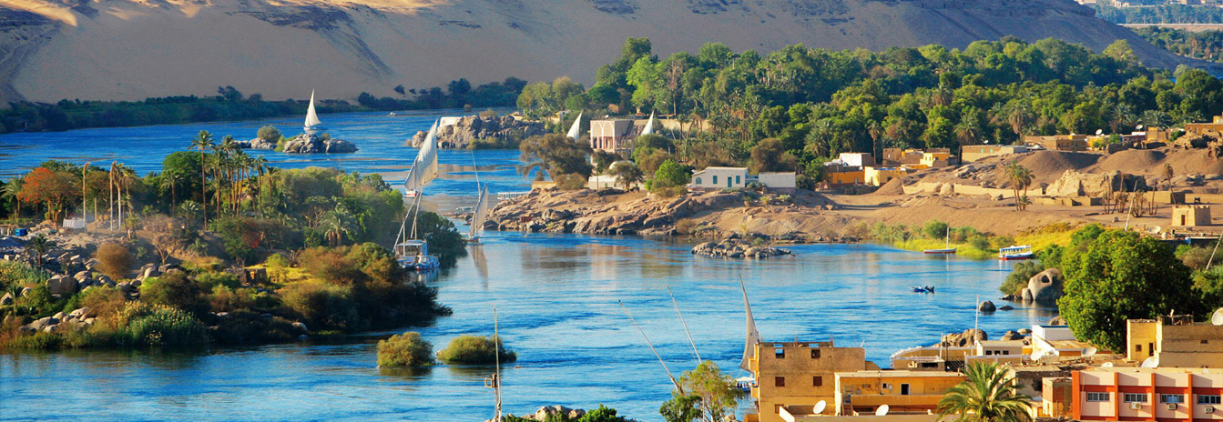 A traditional white-sailed Felucca boat cruising the Nile River at sunset in Upper Egypt